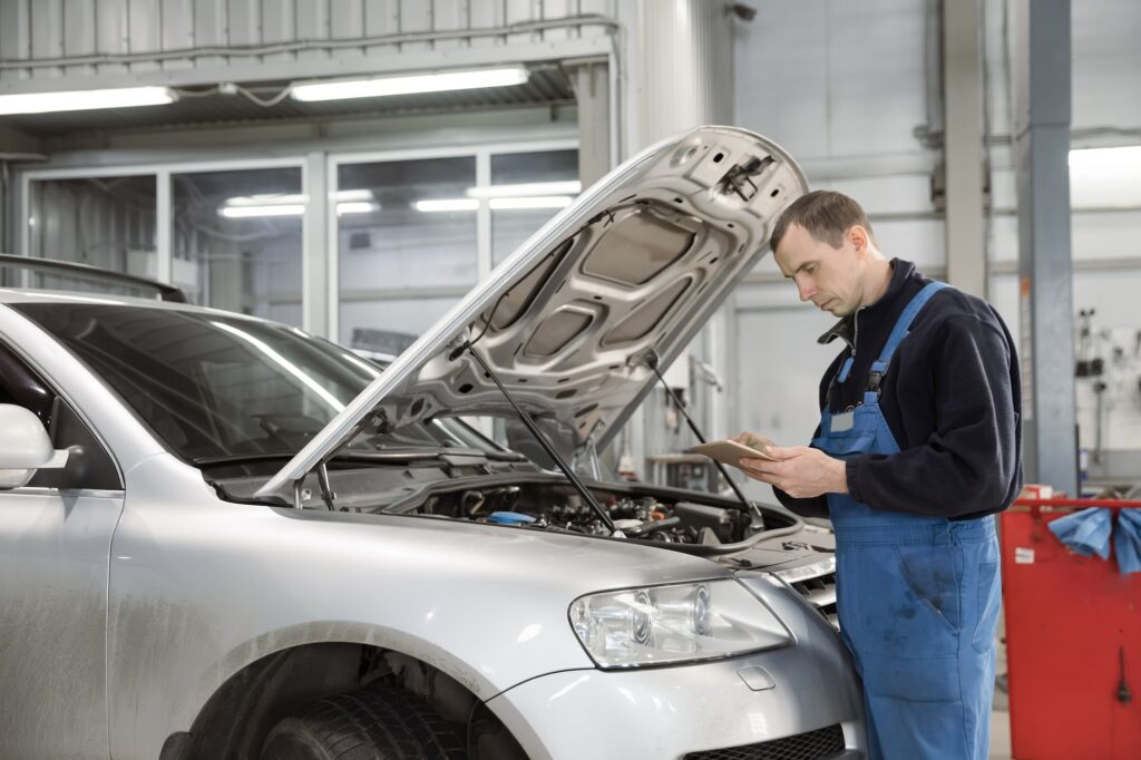 Car mechanic standing in front of the open hood with a diagnostic tablet